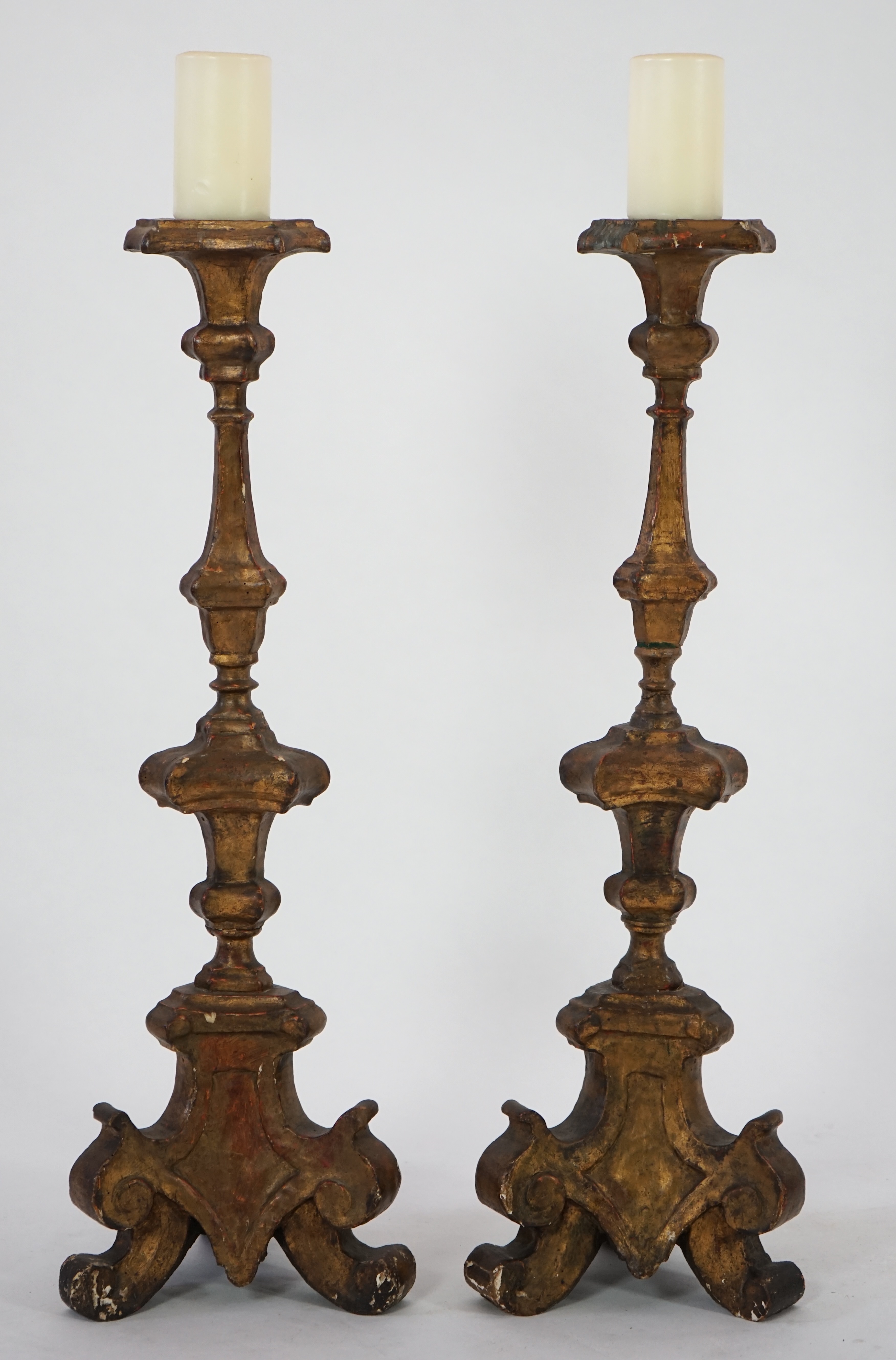 A pair of 18th century Italian giltwood candlesticks with knopped triangular stems and scroll feet, 89cm high. Condition - fair, Provenance- Brede Place, East Sussex, a former residence of the Frewen family from 1712-193